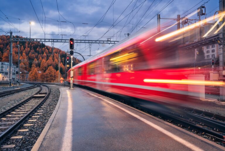 Blurred,Red,Passenger,Train,Passing,Mountain,Railway,Station,During,Rain